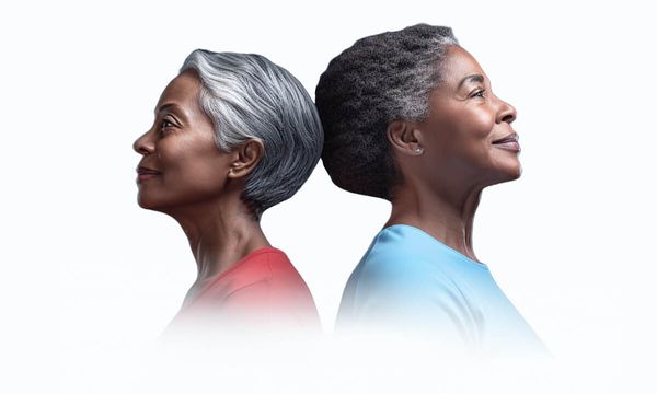 Two senior woman with short grey hair standing back to back smiling outward.