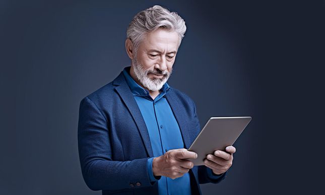 Senior man in a sport coat looking down at a tablet in his hands.