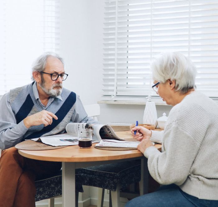 Senior couple sitting at table drinking coffee and reading the newspaper.