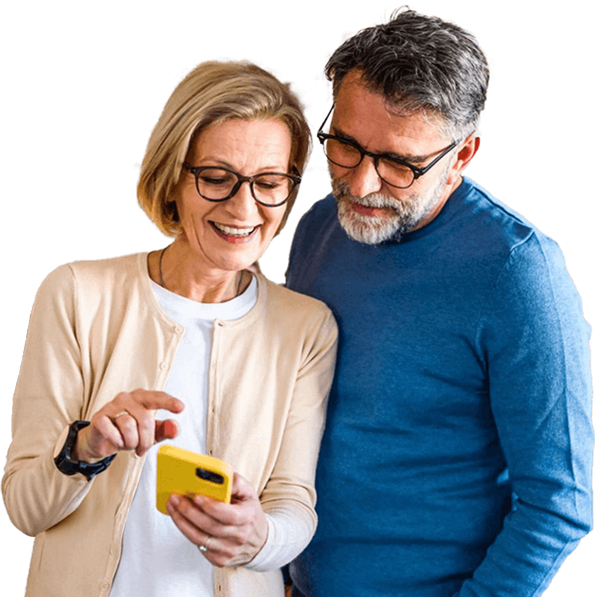 Mature couple standing side-by-side smiling down at a mobile phone.
