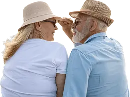 Senior couple wearing sunglasses and straw hats smiling at each other.
