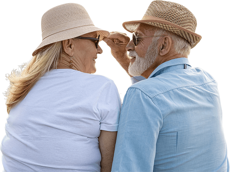 Senior couple wearing sunglasses and straw hats smiling at each other.