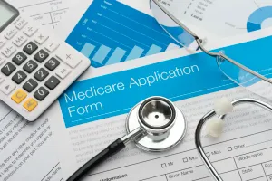 Medicare enrollment forms spread out on a table with a calculator and some glasses.